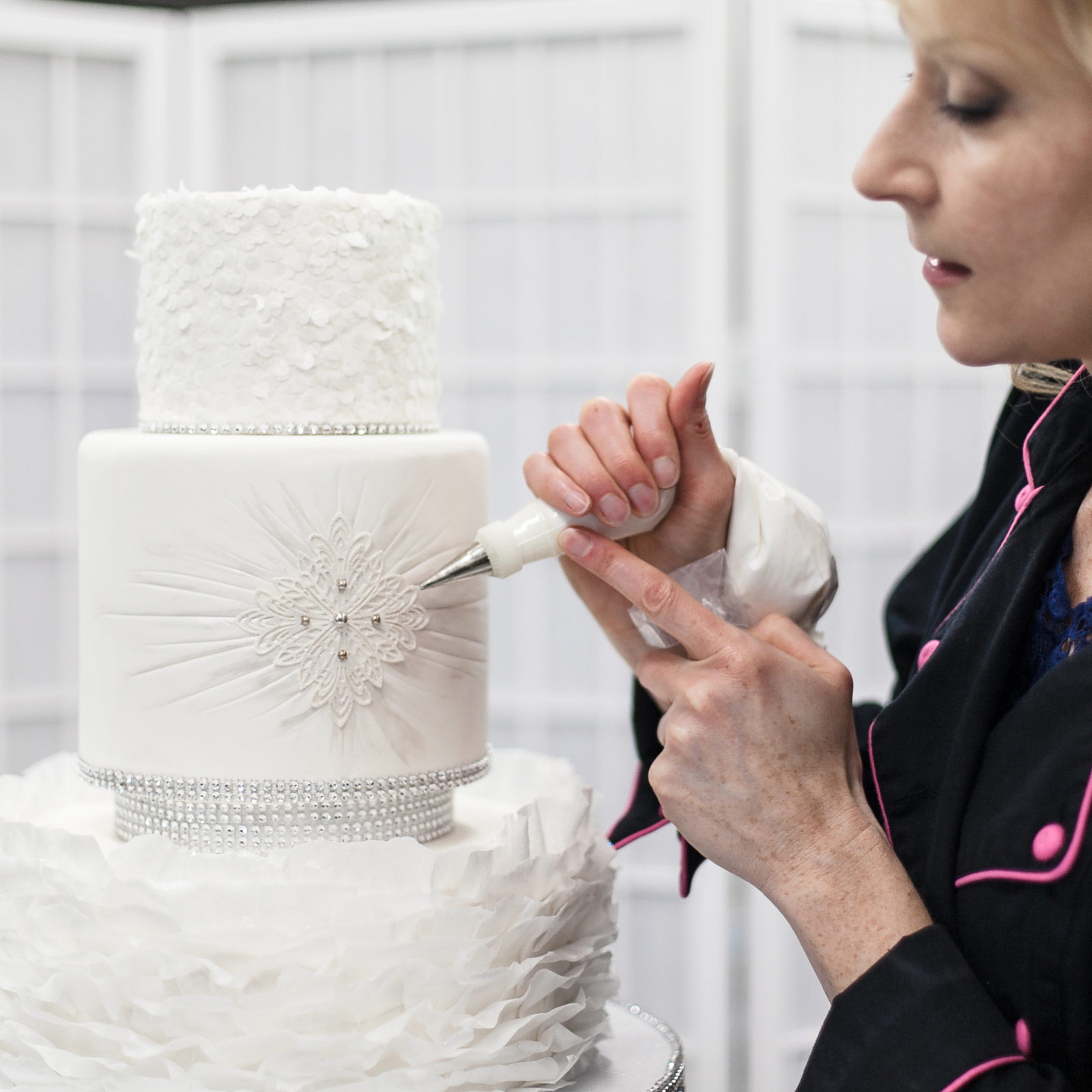 A woman putting icing on a wedding cake.
